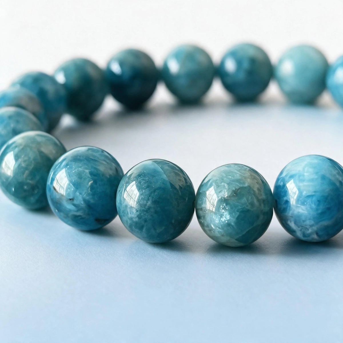 Macro close-up of authentic natural blue apatite beads showing oceanic mineral banding and silky sheen by Ember Quiet.
