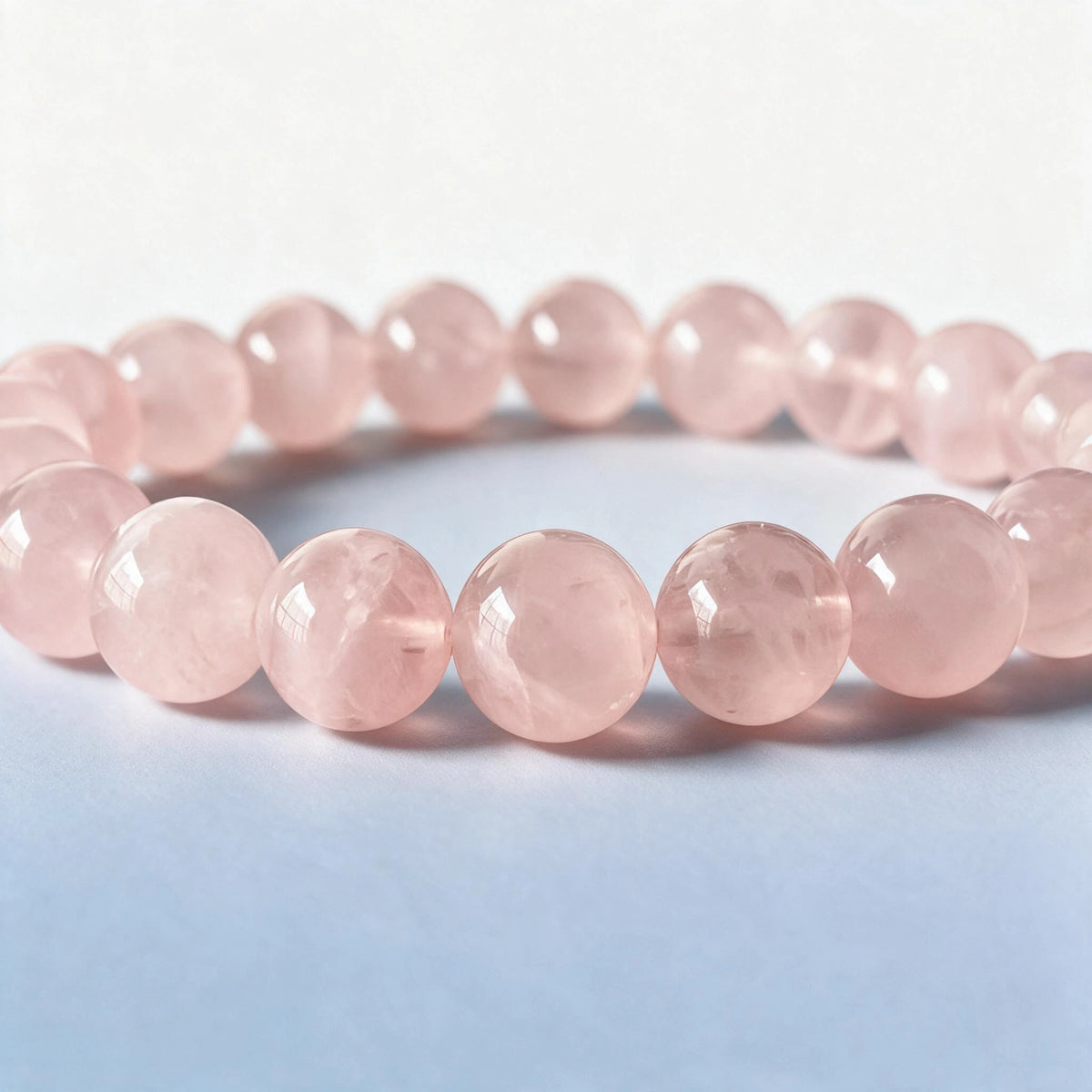 Macro close-up of authentic natural rose quartz beads with translucent crystal veils and blush luster by Ember Quiet.