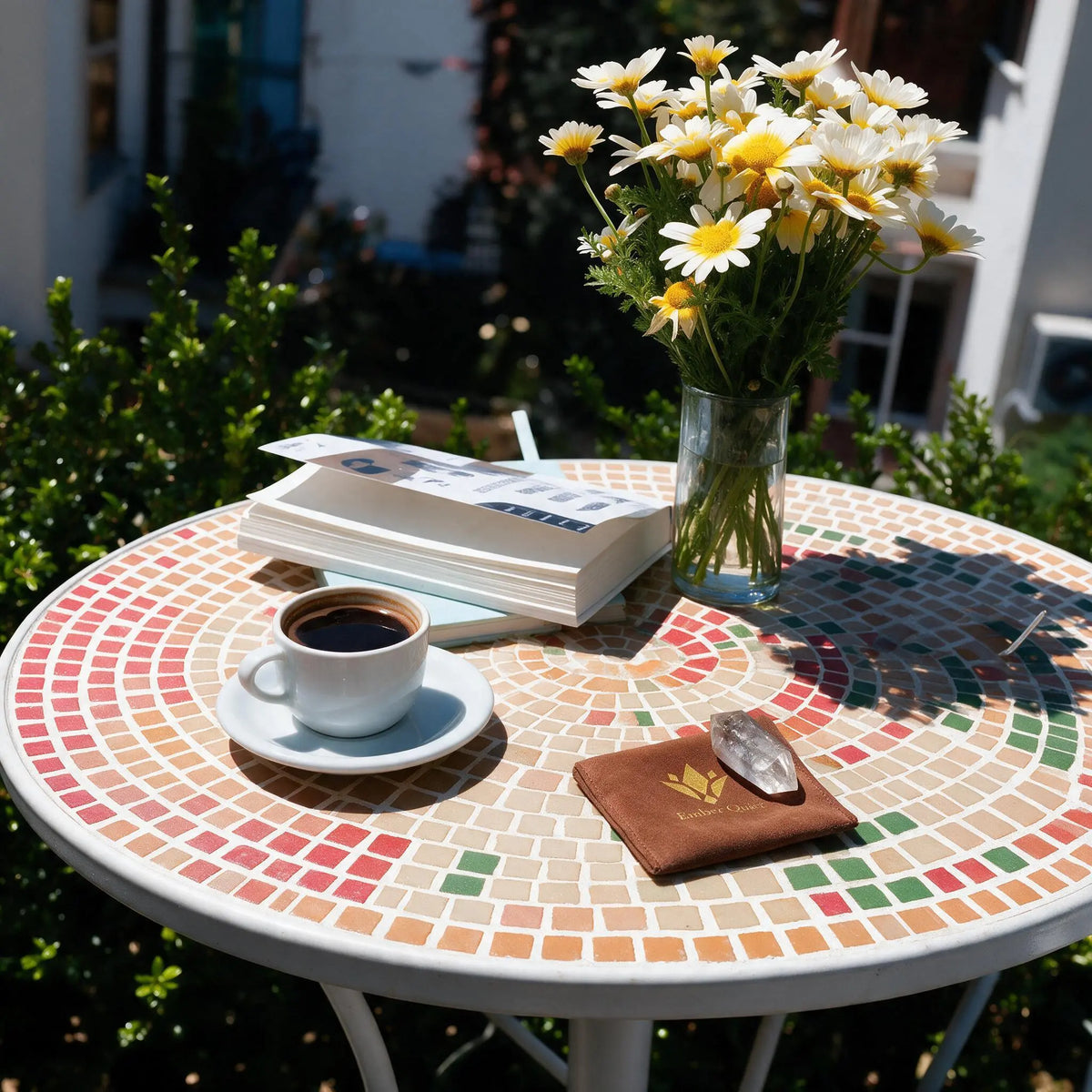 An Ember Quiet clear quartz crystal resting on its brown velvet pouch on a sunny outdoor table with a coffee cup and a book. Take a moment for mindful rest, recharging both your physical and mental energy.