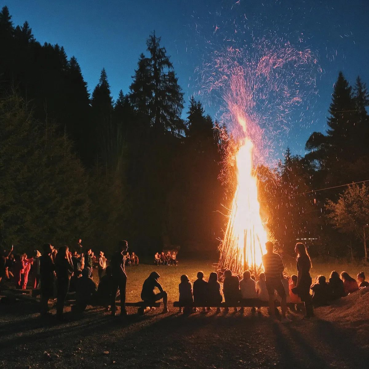 People sitting around a warm forest bonfire at night, sharing the quiet joy of passing embers by Ember Quiet.